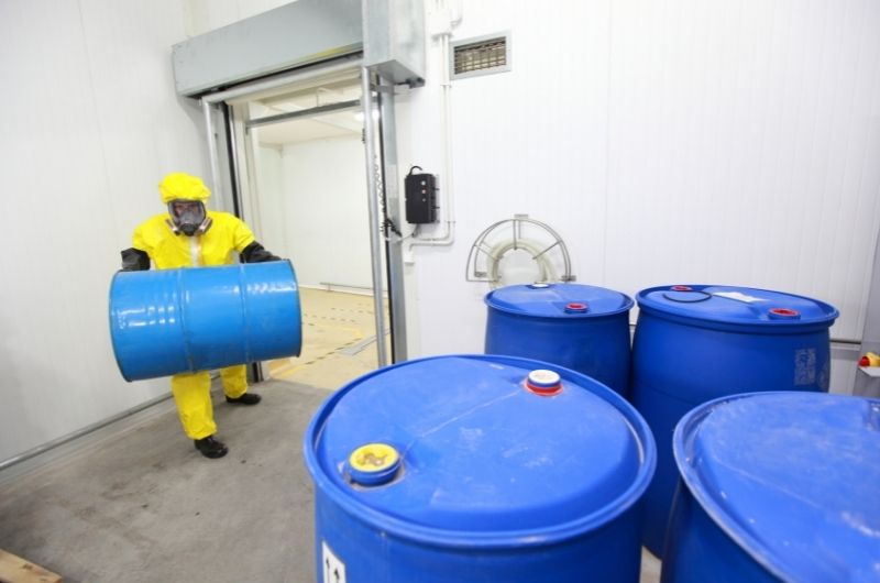 worker in hazmat suit with chemical barrels