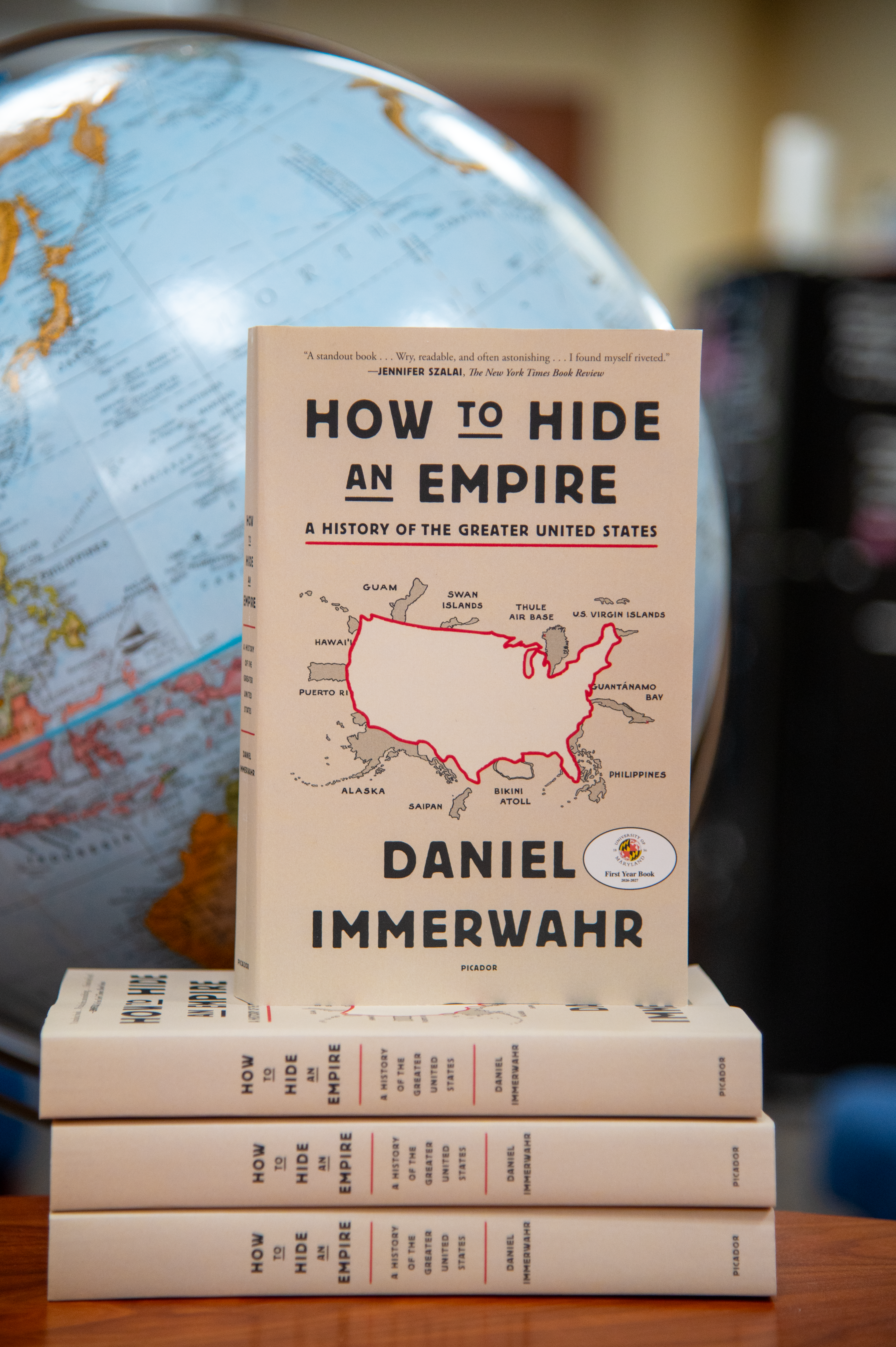 stack of How to Hide an Empire Books in front of globe